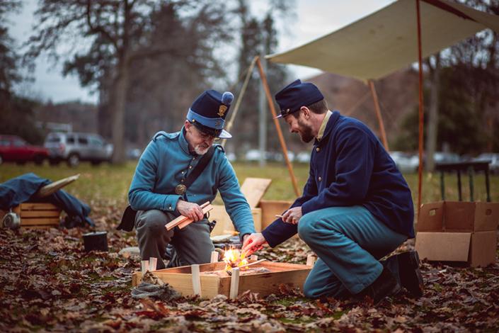 A two men in old military attire around a small campfire