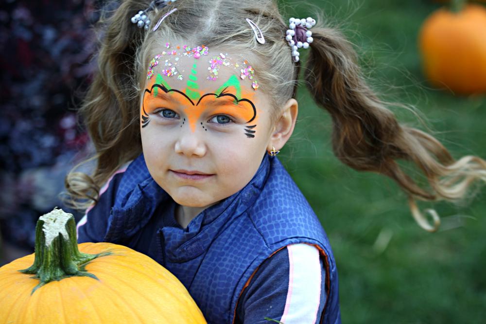 Little girl with face paint smiles while holding a pumpkin.